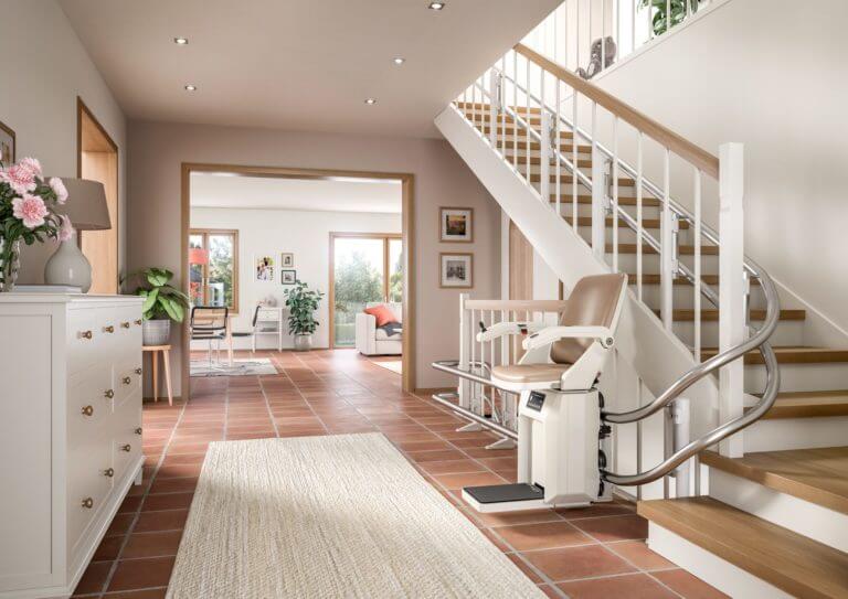 Barrierefreier Treppenlift im modernen Wohnambiente, der den Zugang zu oberen Etagen erleichtert. Heller Eingangsbereich mit Fliesenboden, Treppe und stilvollen Möbeln. Ideal für Senioren und Menschen mit Mobilitätseinschränkungen.