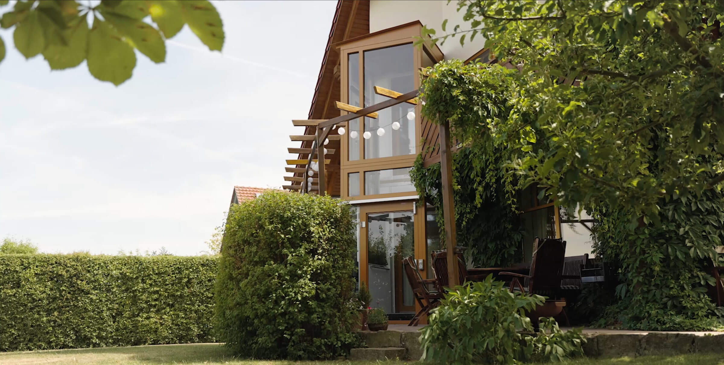 Modernes Holzhaus mit großen Fenstern, umgeben von üppigem Grün und einem gepflegten Garten. Ideal für naturnahe Wohnideen und entspannte Ausblicke.