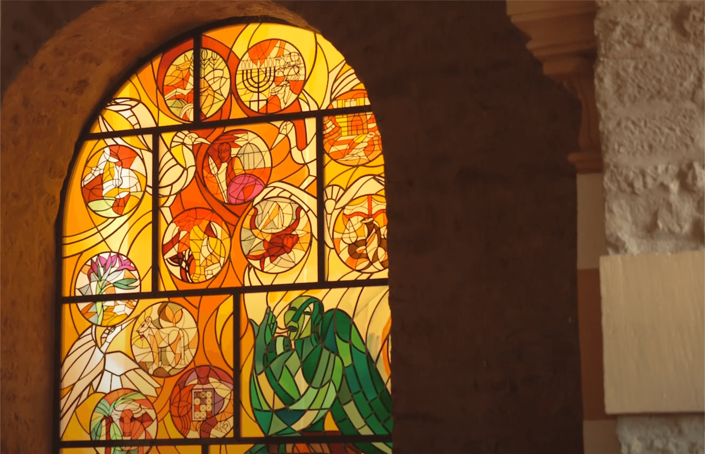 Buntes Kirchenfenster mit geometrischen und figürlichen Motiven, das Licht in warmen Farbtönen durchlässt und eine spirituelle Atmosphäre schafft.