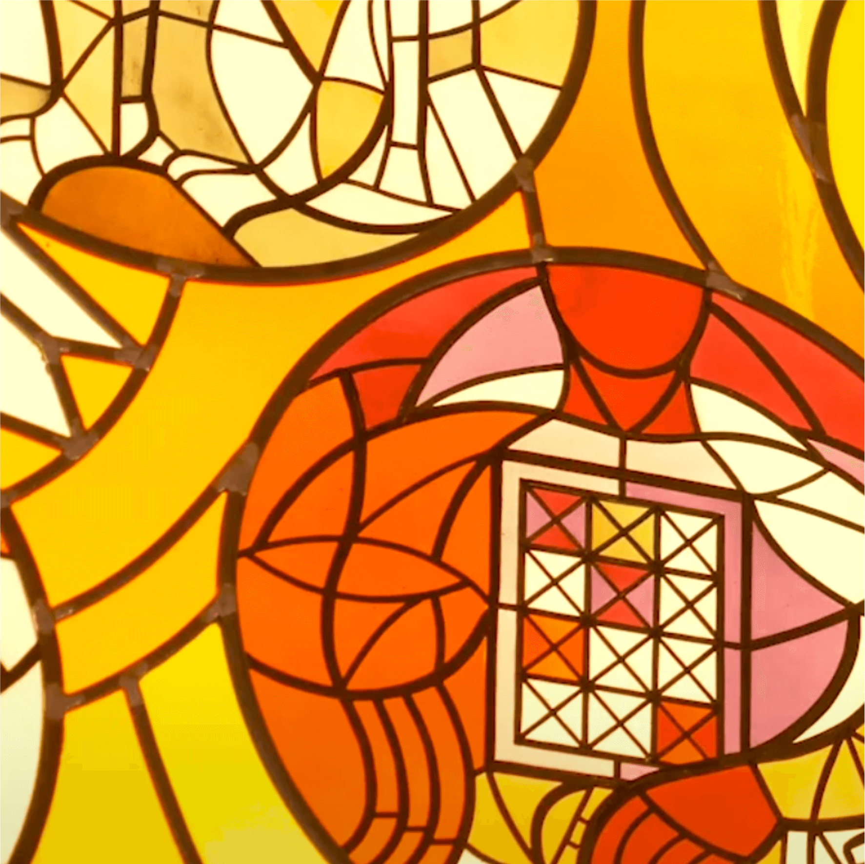 Buntes Glasfenster mit geometrischen Mustern in warmen Farbtönen von Gelb, Orange und Rot, das kunstvolle Lichtspiele erzeugt.