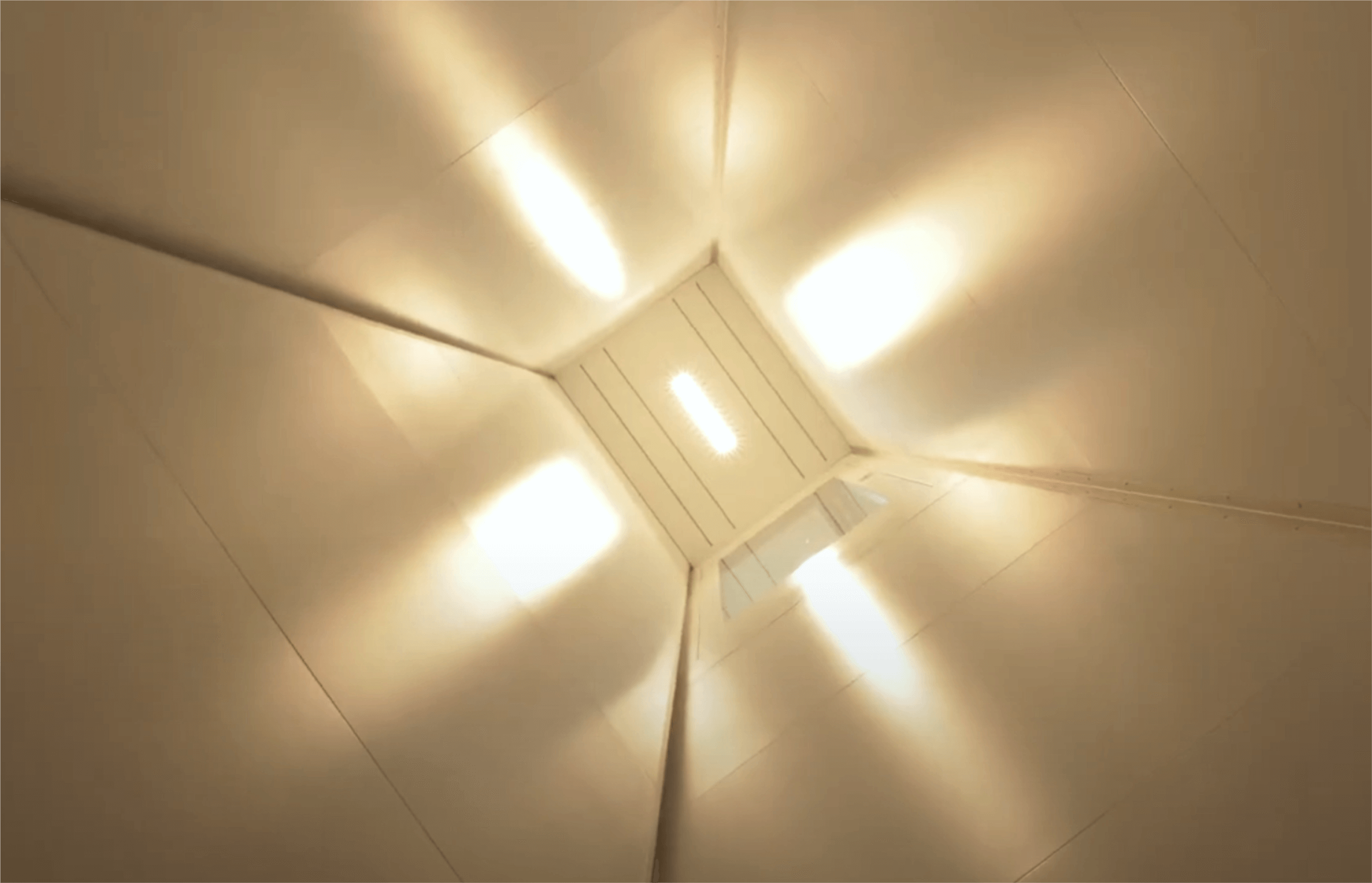 Blick auf die Decke eines modernen Raums mit strahlenden Deckenleuchten, die eine warme Atmosphäre schaffen. Die symmetrische Anordnung der Lichter sorgt für eine gleichmäßige Ausleuchtung.