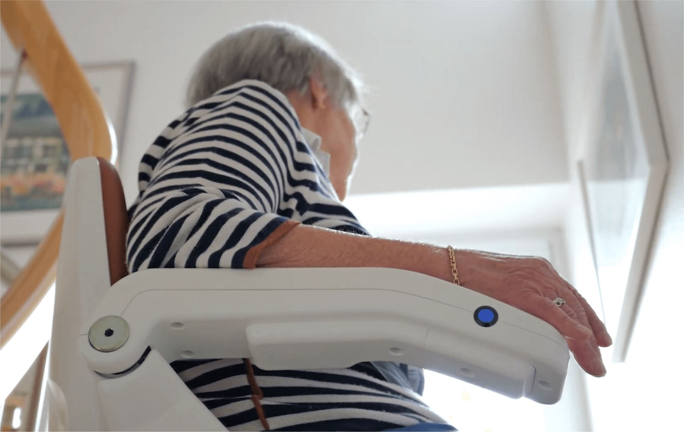 Seniorin sitzt auf einem Treppenlift und blickt nach oben, während sie sich in einem Wohnbereich mit Treppe befindet. Der Fokus liegt auf der komfortablen und sicheren Nutzung des Treppenliftes.